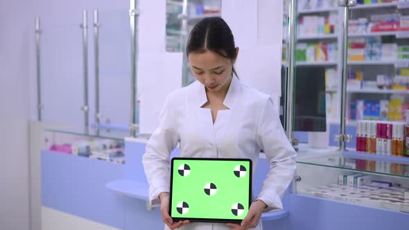 Young Asian Woman Posing with Green Screen Digital Tablet at Cash Desk in Pharmacy