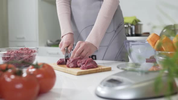 Woman Cutting Raw Meat on Small Pieces with Kitchen Knife Cutting Board. Woman Puts Pieces of Raw