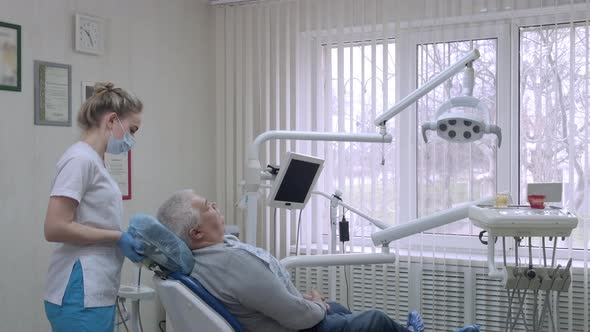 Dental Assistant Wearing Protective Mask Prepares Elderly Patient for Checkup at Dental Clinic Sets