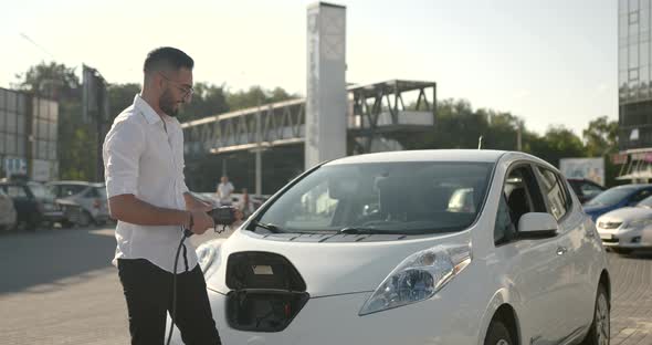 Young Arab Man Recharging White Electric Car at Parking Lot