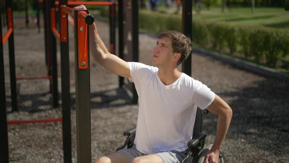 Portrait of Inspired Young Man in Wheelchair Looking Up at Gymnastic Set Sitting in Sunshine