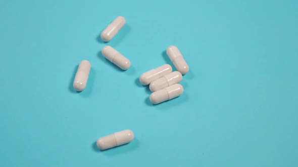 White medical capsules fall on a blue paper bright surface. 