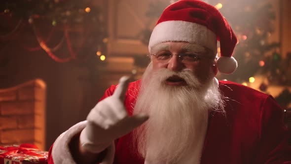 Old Kind Santa Is Sitting in His Room in Residence at Christmas Holiday, Holding Finger Near Lips To