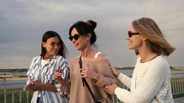 Three young women in sunglasses walk along the waterfront