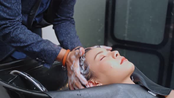 Asian young woman laying on salon washing bed getting hair washed in hair salon by stylist.
