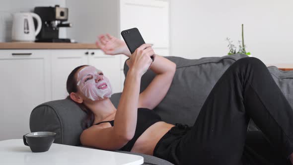Young Millennial Woman at Home Applying Cloth Mask on Face and Doing Video Call. Wellness Relaxing