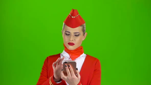 Stewardess in the Red Attire Looks Into the Phone and Is Surprised. Green Screen