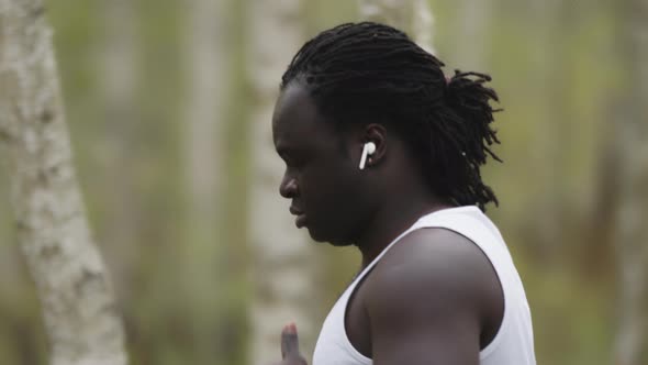 Weight Loss Concept. An African Man Running in the Forest with Wireless Headphones. Slowmotion