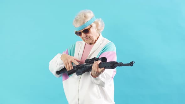 Old Woman in Sportswear and Black Sunglasses Is Holding a Rifle Isolated on Blue