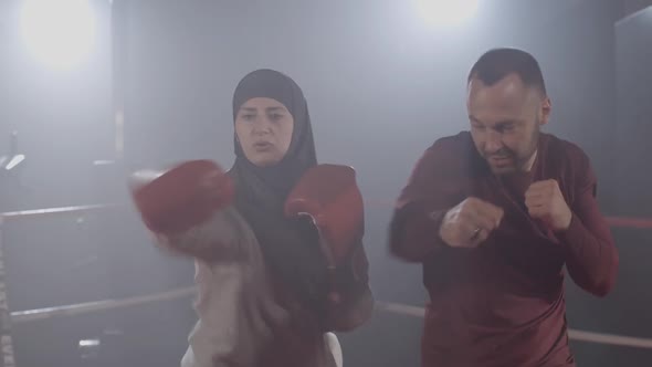 Focused Muslim Woman Punching Air As Trainer Endorsing Female Boxer on Boxing Ring. Portrait of