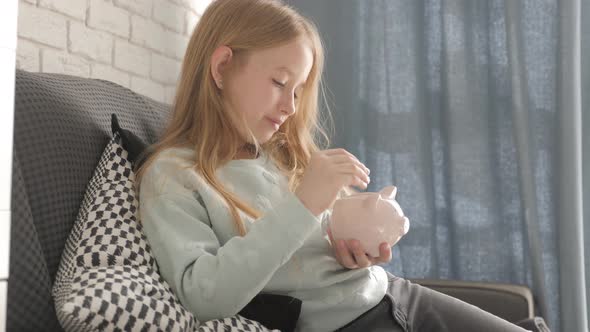 Happy Girl Save Money in Piggy Bank in Her Home. Child Inserting a Coin Into a Piggy Bank, Indoor