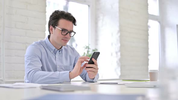 Cheerful Working Young Man Using Smartphone in Office