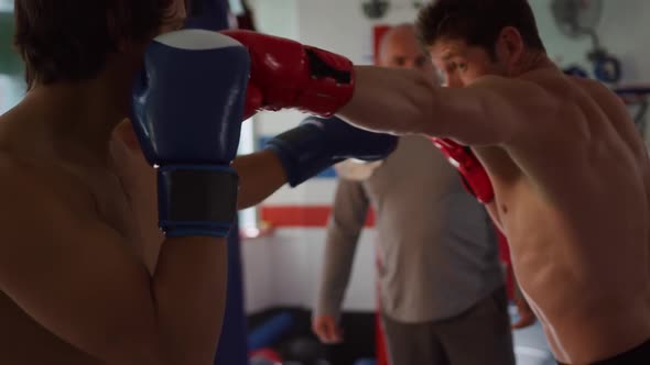 Two caucasian men boxing with a coach in boxing ring