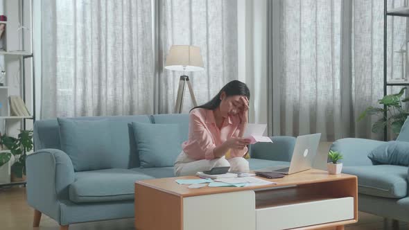 Asian Woman With A Laptop Looking At The Bill And Having A Headache Due To Financial Problem