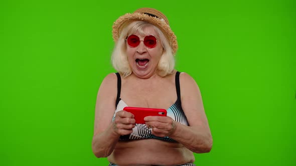 Senior Addicted Woman Tourist in Red Sunglasses Enjoying Smartphone Gadget Video Games on Chroma Key