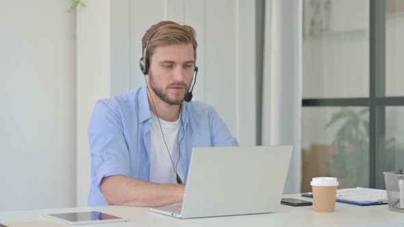 Creative Man Talking on Headset Working on Laptop in Office