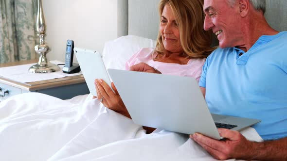 Happy senior couple on bed using laptop and digital tablet