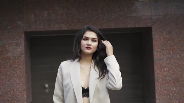 Stylish Brunette in a Bra and Coat Seductively Walks Posing in the Parking Lot