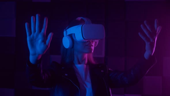 Young Woman in Futuristic VR Headset Gesturing with Hand While Interacting with Cyberspace Under