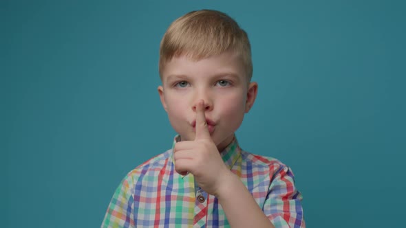 Preschool Boy Showing Silence Sign with Forefinger By Mouth Standing on Blue Background