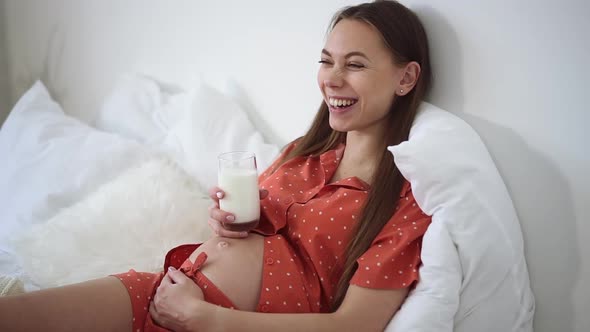 Portrait of Positive Pregnant Woman Laughing and Holding Glass of Milk Spbd