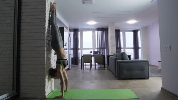 Young Fit Woman Doing Handstand Near Wall at Home