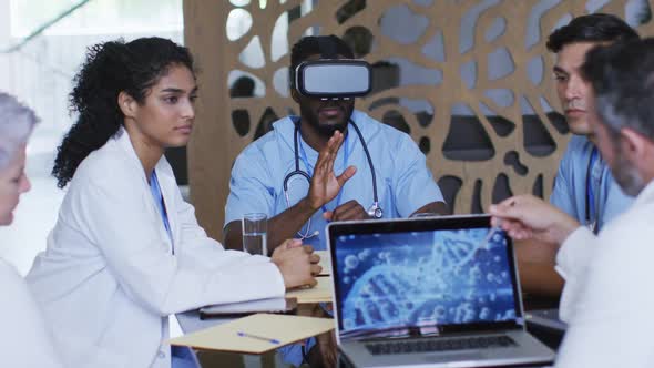 Diverse group of doctors sitting in discussion at a meeting using laptop and vr headset