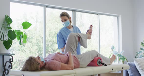 Female health worker stretching leg of senior woman at home