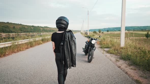 Stylish Motorcyclist Woman in Helmet and Leather Jacket Walking to Her Retrostyled Motorcycle