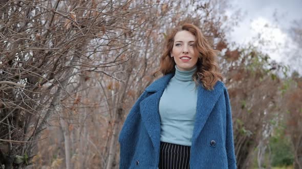 Young Redhaired Woman in a Blue Coat and Walks Against the Backdrop of the Old City