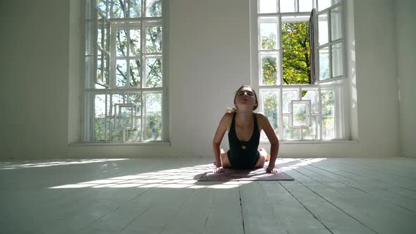 Red-haired Young Healthy Caucasian Woman Practicing Yoga on the Mat in the White Large Room