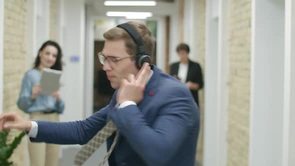 Joyful Young Businessman Dancing in Headphones As Blurred Colleagues Recording Video on Gadgets at