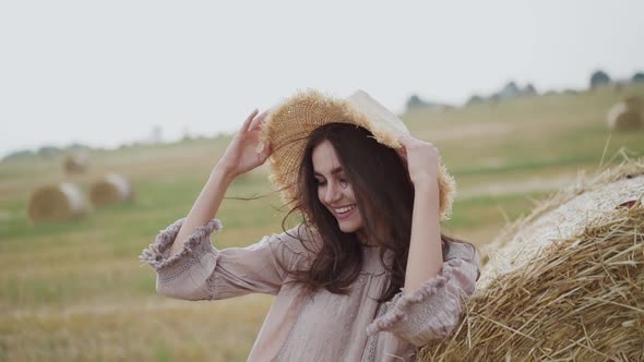 Happy Young Girl Putting Hat on Blowing Hair at Haycock in Windy Field