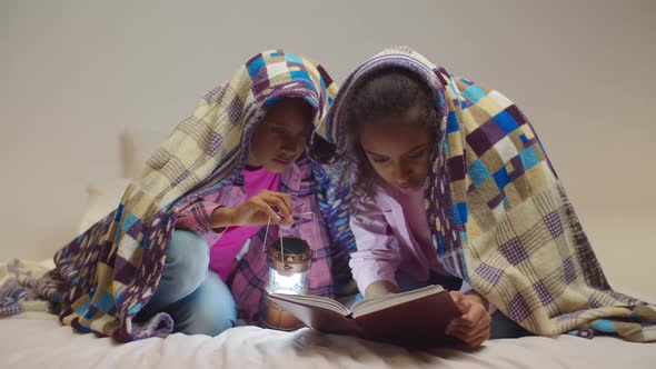 Elementary Age Sisters Reading Book Under Blanket