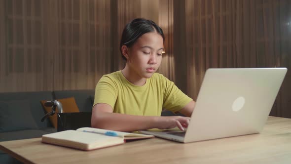 Asian Kid Girl Sitting In A Wheelchair While Using Laptop Computer At Home