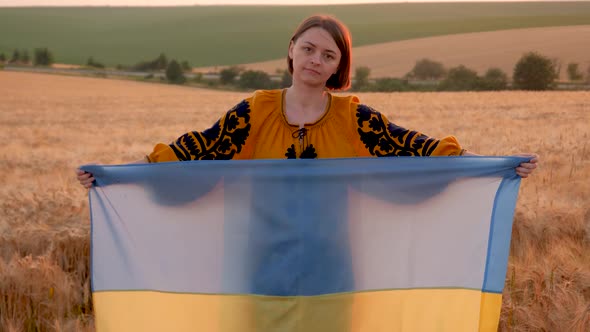 a woman in an embroidered shirt in a wheat field with a blue-yellow flag of Ukraine