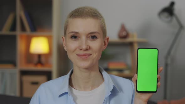 Smiling Woman Holding Smartphone with Green Screen at Home