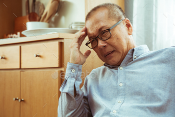  – close up of Asian senior man  sitting on sofa and having headache at home.he may had Headache Symptoms.She looks pain  and sick