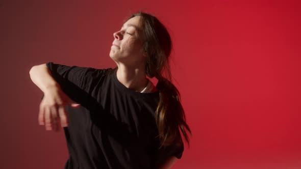 Brunette Woman Wearing Black Tshirt Dancing Contemporary on Red Neon Background in Studio