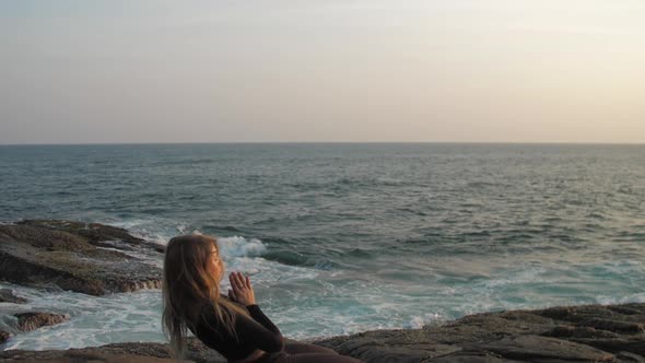 Young Woman in Black Tracksuit Stretches on Grey Rocky Cliff