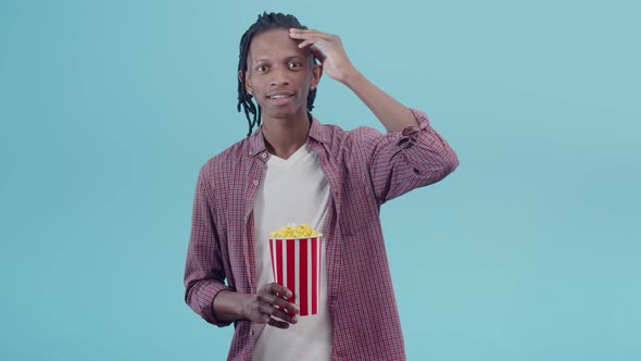 Black man holds a paper cup with popcorn in hand and is surprised to be looking at the camera
