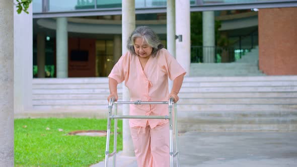 Happy old elderly Asian woman uses a walker and walks in the hospital after recovering from an accid