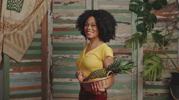 Young Stylish African American Woman with Basket of Fresh Exotic Fruit Walking and Smiling to Camera