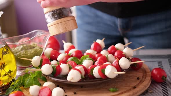 Pouring Grinded Pepper on Caprese Canapes with Cherry Tomatoes and Mozzarella Cheese Balls