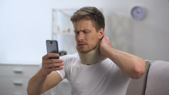 Man in Foam Cervical Collar Reading Message on Cellphone, Feeling Pain in Neck