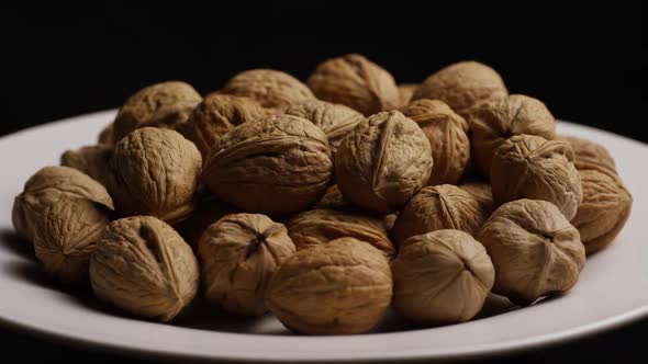 Cinematic, rotating shot of walnuts in their shells on a white surface 