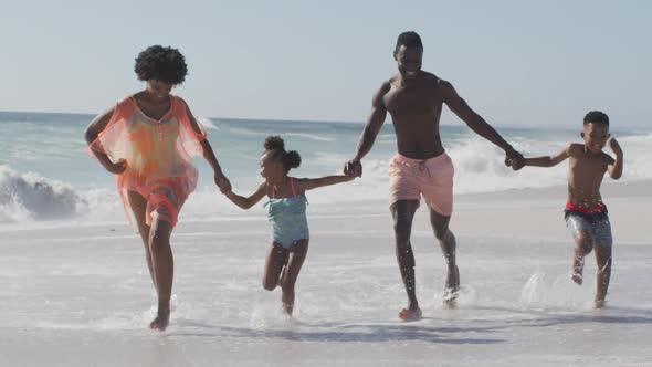 Smiling african american family holding hands and running on sunny beach