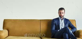 cessful businessman is sitting on sofa at office and waiting somebody. Business look. Fashion portrait.