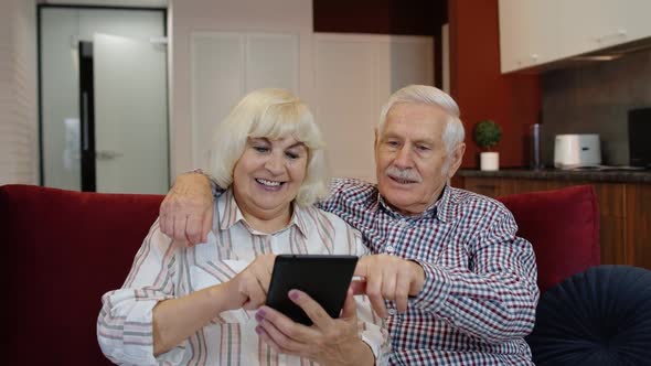 Senior Old Couple Grandparents Talking and Using Digital Tablet Computer at Home. Internet Shopping