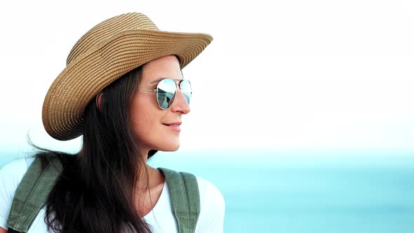 Portrait of Pensive Young Woman in Sunglasses and Hat with Backpack Enjoying Amazing Seascape